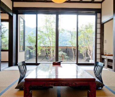 Traditional tatami room with low lacquered table, legless chairs and large sliding doors opening to garden and distant hills