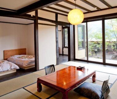 Japanese tatami room with low table, cushions, futon bedding and garden-facing sliding doors at Yamakikan Gunma