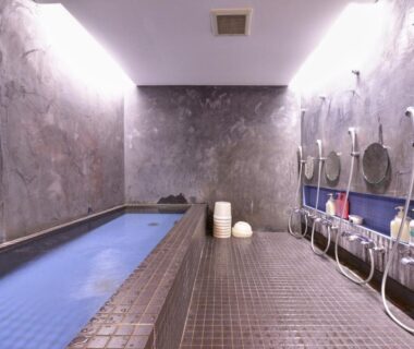 Stone-lined indoor communal bath with shower stations and tiled floor at Yamamoto Ryokan in Kyoto