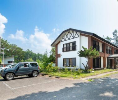 Two-story ryokan exterior with parking and trees at Yamanaka Lake Ryozan, Yamanashi