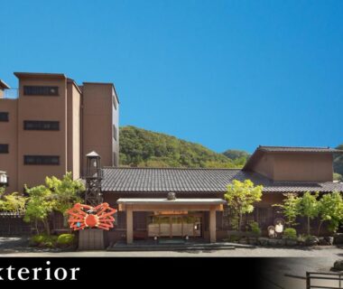 Front entrance and facade of Yamanaka Onsen Kagari Kisshotei with multi-story building and mountain backdrop in Ishikawa