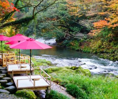 Riverside wooden platforms with pink umbrellas beside flowing river at Yamanaka Onsen Kajikaso, Ishikawa