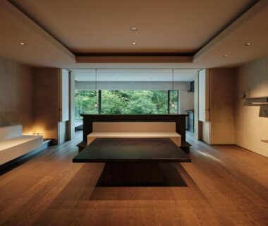 Minimalist Japanese guest room with low platform bed, wooden floors and large window overlooking garden greenery at Yamanakaonsen Hanamurasaki