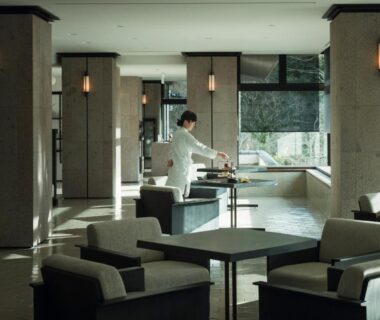 Spacious lounge with armchairs and staff arranging tea at Yamanakaonsen Hanamurasaki in Ishikawa