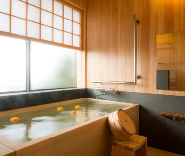 Wooden soaking tub with floating citrus, shoji screens and warm wooden walls at Yamanoo ryokan in Ishikawa