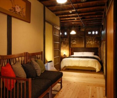 Warm wooden interior bedroom with bed, sofa, cushions and exposed ceiling beams at Yamasaki Ryokan Q Nakamonzenya Hyōgo