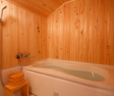Wood-paneled bathing area with tub and wooden stool at Yamasaki Ryokan Q Nakamonzenya in Hyōgo