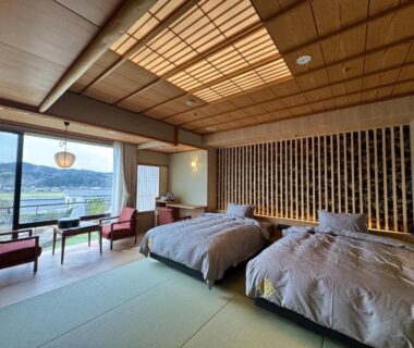 Tatami room with twin beds, low seating by large window overlooking valley at Ishikawa ryokan