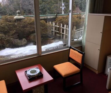 Seating area with low table facing garden lantern and light snow at Yamashiro Onsen Yuzankaku