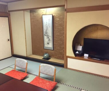 Traditional tatami room with low table, zabuton cushions, tokonoma scroll and television at Yamashiro Onsen Yuzankaku, Ishikawa