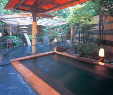 Covered outdoor wooden onsen bath with stone paving, lanterns and garden at Yamashiro Onsen Yuzankaku Ishikawa