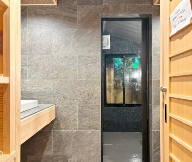 Wooden sliding door leading to stone-tiled bathing area with sink and glass window