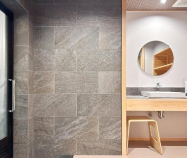 Stone tile wash area with sink, round mirror, wooden stool and frosted glass door at Yamatoya, Hyōgo, Kansai