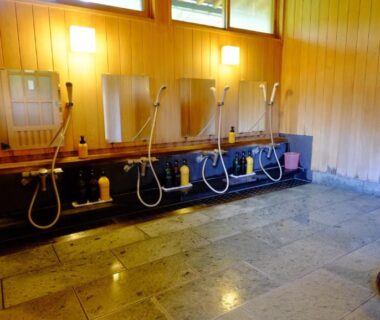 Wood-paneled wash stations with handheld showers, stools and buckets in a ryokan bathing area at Yamazatonoiori Soene Gifu