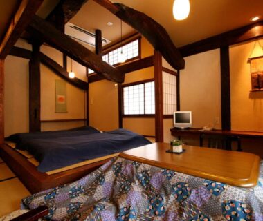 Traditional tatami room with kotatsu, raised bedding platform, shoji screens and wooden beams at Yamazatonoiori Soene in Gifu