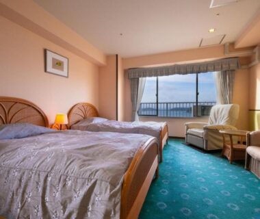 Twin beds with seating area and large window overlooking water at Yanagiya in Wakayama