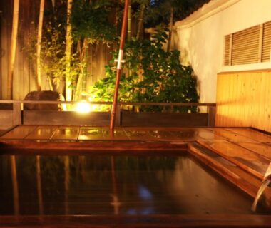 Wooden onsen bath with warm ambient lighting and garden foliage at Yanagiya in Yamanashi