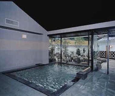 Covered stone onsen pool with glass wall and tiled floor at Yanagiya, Yamanashi