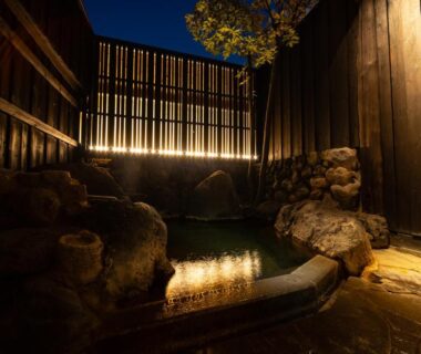Nighttime outdoor stone onsen with wooden fence and warm lighting at Yasuraginoyado Yufu in Oita, Kyushu