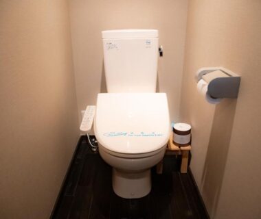 Compact restroom with bidet-equipped toilet, dark wooden floor and small stool at Yasuraginoyado Yufu, Ōita