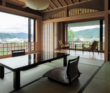 Tatami room with low lacquer table, zabuton cushion, shoji screens and balcony overlooking green hills at Yatsusankan, Gifu