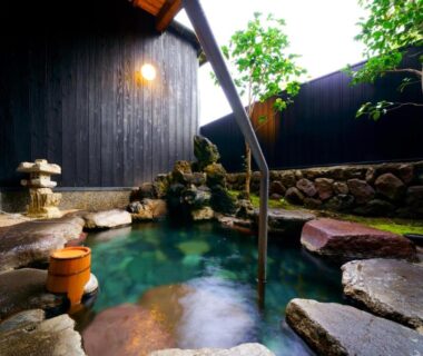 Stone-lined outdoor onsen with wooden bucket and handrail at Yawaragi-no-Sato Yadoya, Ōita