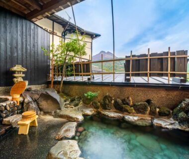 Outdoor stone onsen with wooden stools and bamboo fence at Yawaragi-no-Sato Yadoya in Ōita, Kyūshū