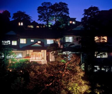 Illuminated traditional ryokan exterior at dusk with lit windows and surrounding trees in Shizuoka, Chūbu