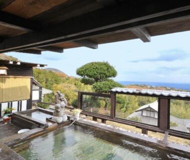 Wooden outdoor onsen baths with covered roof and distant coastal horizon at Yokohama Fujiyoshi Izuten Shizuoka
