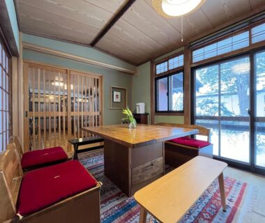 Tatami room with low wooden table, red cushions, shoji screens and large windows with trees outside at Yokokura Ryokan Nagano
