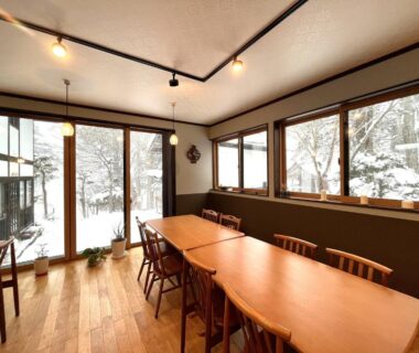 Long wooden dining table and chairs by large windows overlooking snow-covered trees at Yokokura Ryokan, Nagano