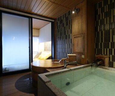 Indoor stone onsen bath and wooden tub beside shoji doors with futon bedroom beyond, Yorokobinoyado Takamatsu, Gunma