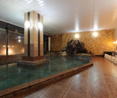 Spacious tiled indoor onsen with row of shower stools and central soaking pool at Yorokobinoyado Takamatsu, Gunma