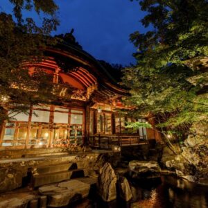 Lit traditional wooden ryokan entrance with stone steps and garden pond, evening at Yorozuya in Nagano