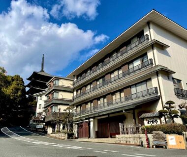 Multi-story ryokan exterior with pagoda in background under blue sky at Yoshidaya Ryokan, Nara, Kansai
