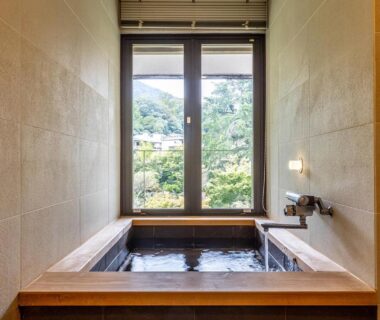 Indoor wooden bath with large window and green hillside view at Yoshiike Ryokan in Kanagawa, Japan