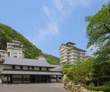 Exterior view of Yoshikawaya with low wooden façade and taller guest wing, tree-lined courtyard in Fukushima, Tōhoku
