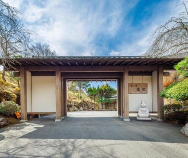 Wooden ryokan entrance with open gate, stone driveway and manicured garden at Yoshimatsu in Kanagawa