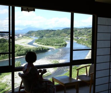Guest in yukata seated by shoji window overlooking riverside and mountains at Yoshinotei, Nagano