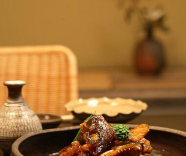 Simmered fish dish in ceramic bowl with sake carafe on low table, rattan chair and vase in Yoyokaku Saga Kyushu