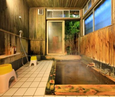 Indoor wooden onsen bath with tiled washing area and stools at Yudanaka Seifuso Nagano