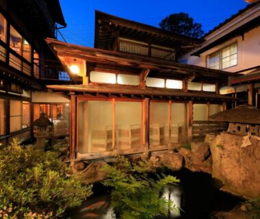 Traditional wooden ryokan courtyard with pond and illuminated shoji windows at dusk, Yudanaka Seifuso, Nagano