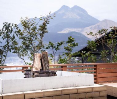 Rectangular outdoor bath on wooden terrace with mountain backdrop and surrounding greenery at Yufudake Ichibo no Yado Kirara
