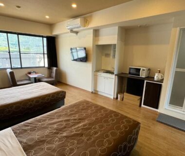 Twin beds with seating area, TV, kitchenette and window overlooking greenery at Yufuin Akarinoyado, Ōita