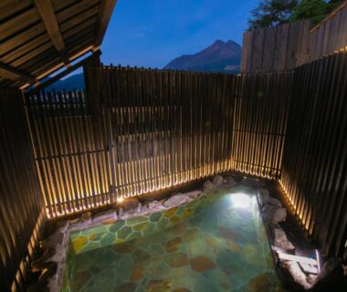 Enclosed outdoor stone onsen with bamboo fence and evening sky at Yufuin Bath Satoyamasafu, Ōita, Kyūshū
