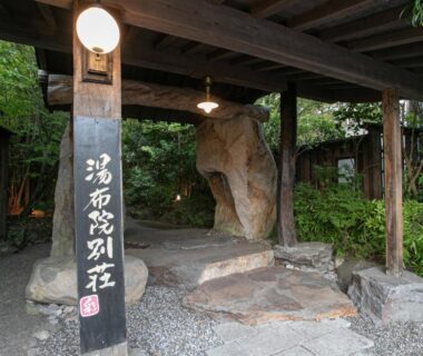 Covered wooden entrance with stone steps, lantern and vertical sign at Yufuin Besso Shikisai in Ōita, Kyūshū