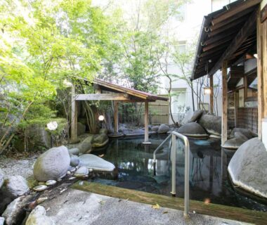 Rock-lined outdoor onsen with wooden shelter at Yufuin Besso Shikisai Hotel in Ōita, Kyūshū