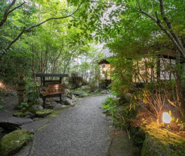 Stone garden path with lanterns and lush greenery leading to ryokan building at Yufuin Besso Shikisai, Ōita