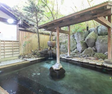 Outdoor stone onsen bath with wooden pergola and bamboo fence at Yufuin Besso Shikisai Hotel Ōita