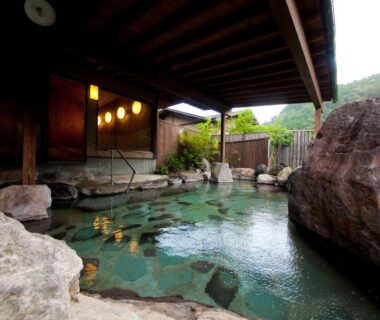 Covered outdoor rock onsen with wooden canopy and garden view at Yufuin Gettouan, Ōita